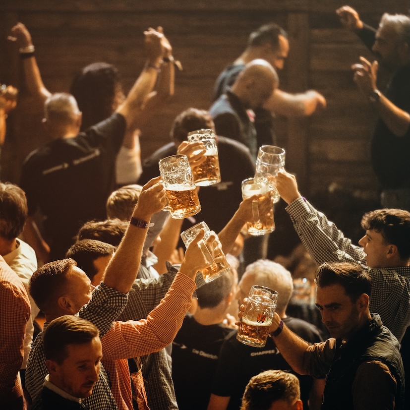 Nahaufnahme mehrerer Gäste, die im WELLER'S Klauss & Klauss Festzelt mit Bierkrügen anstoßen, warmes Bühnenlicht im Hintergrund.