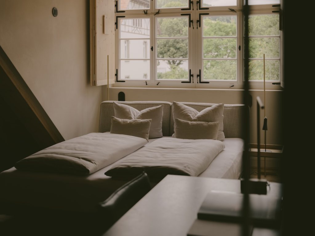 Zimmer im Boutiquehotel 1280 Krone mit Doppelbett vor Sprossenfenstern, Holzläden und Blick auf ein Fachwerkhaus
