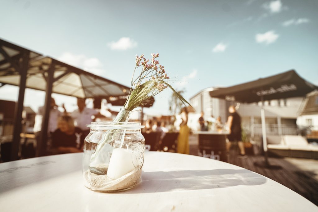 Tischdeko mit Trockenblumen auf der Dachterrasse von OBEN im Tuchhaus, im Hintergrund Gäste bei einem Sommerevent